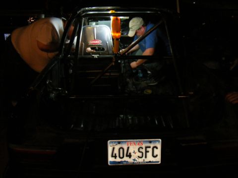 1989 Ford Escort - Mechanics work inside a heavily modified car, likely for racing, a prominent roll cage and racing seat.