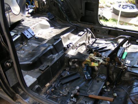 1989 Ford Escort - The interior of a car has been stripped bare, revealing the floor pan and various mechanical components.