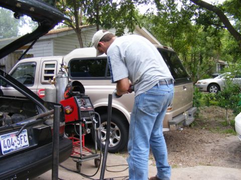 1989 Ford Escort - A person works with welding equipment next to a pickup truck that has a camper shell, with another car visible in the background.