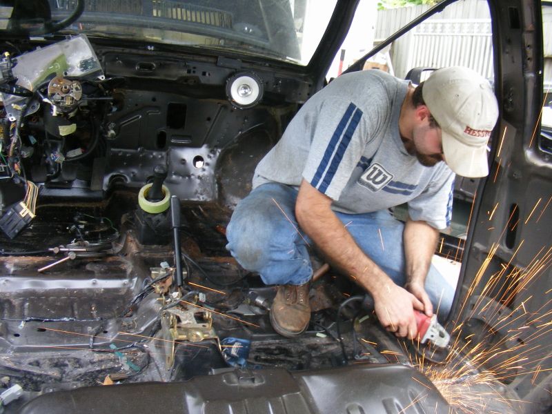 Man grinding metal inside a stripped-down car interior, sparks flying