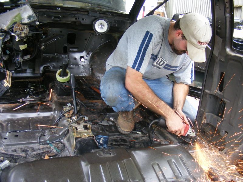 Guy grinding metal inside a stripped-out car interior. Sparks flying everywhere