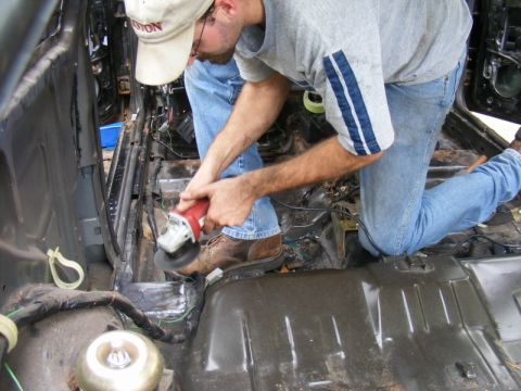 1989 Ford Escort - A person works on the interior of a vehicle, grinding metal and exposing wiring.