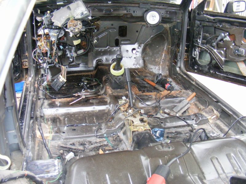 Stripped car interior with exposed wiring and rust