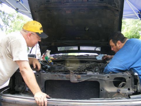 1989 Ford Escort - Men are performing maintenance on a car's engine bay under an open hood.