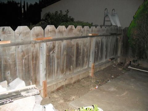 1991 Ford Bronco - A backyard scene shows a weathered wooden fence with a slide peeking over the top, next to a concrete patio area.