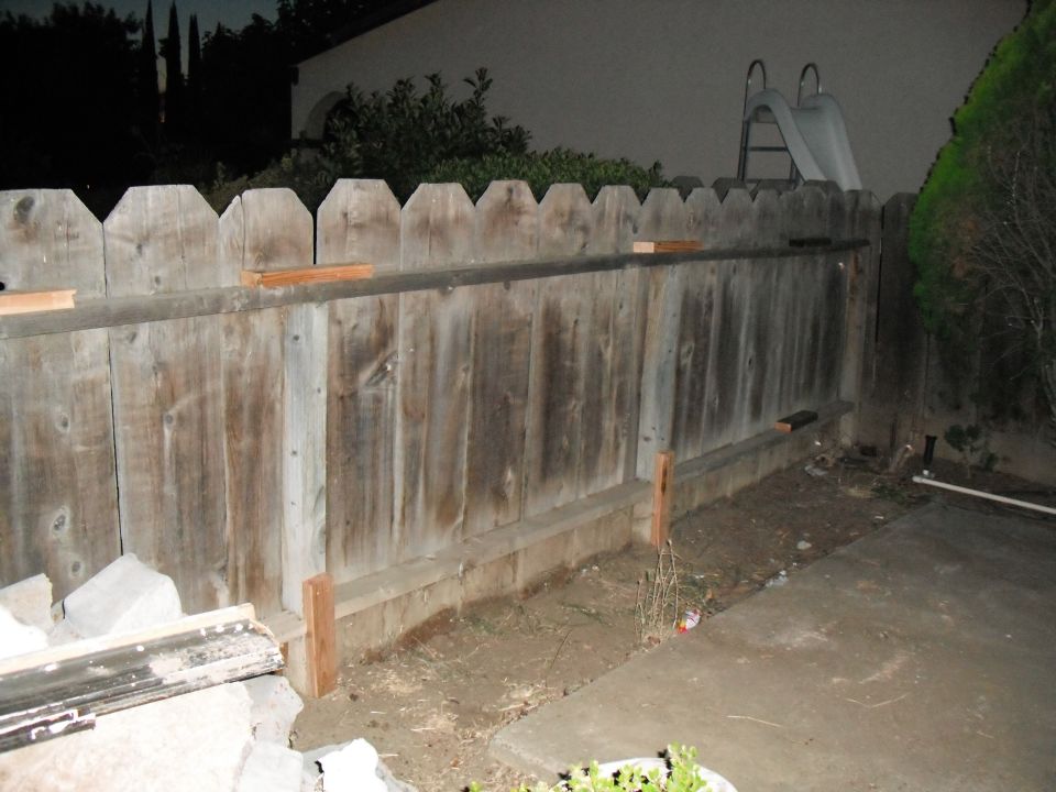 Wooden fence with a slide visible over the top, concrete patio, and some landscaping