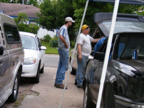 1989 Ford Escort - Two men work on a black pickup truck parked next to a white sedan.