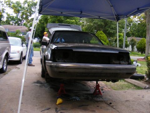 1989 Ford Escort - Car on jack stands with hood open, missing front-end components, parked outside.