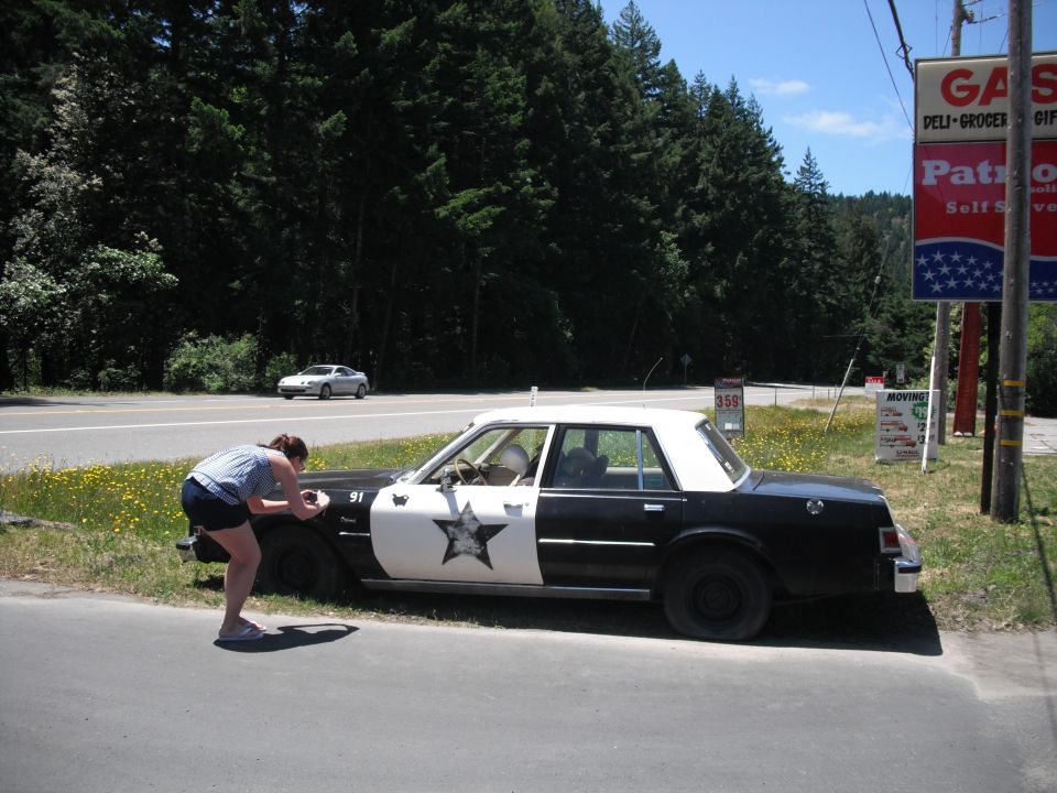 Black and white police car parked on the side of the road with a woman taking a photo of its hood