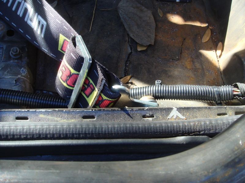 Seatbelt with red and yellow pattern attached to metal bracket, with black wiring harness and corrugated tubing