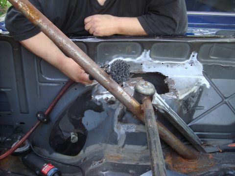 1989 Ford Escort - A person works on the rusted interior of a vehicle, with a roll cage installed.