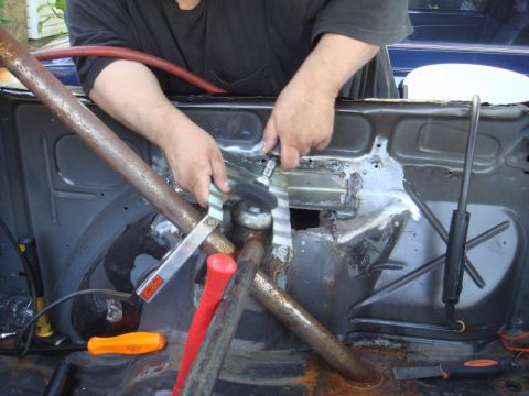1989 Ford Escort - A person grinds metal inside a car's interior, surrounded by a roll cage and tools.