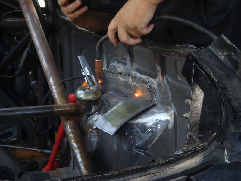 Car body section being welded, showing metal repair work and structural components
