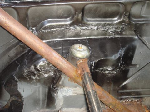 1989 Ford Escort - Close-up of a car's interior chassis, showing a rusty roll cage and black painted floor panels with visible welds.