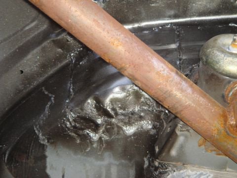 1989 Ford Escort - Undercarriage detail showing a rusty bar and textured black coating with evidence of impact.