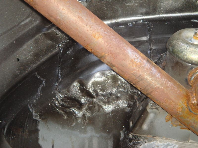 Rusty metal bar over black undercarriage with visible welds and damage