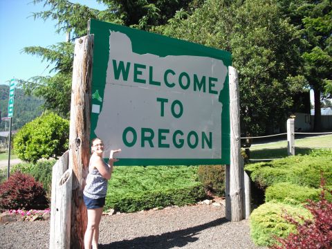 1991 Ford Bronco - A woman poses with the iconic "Welcome to Oregon" sign, marking a memorable stop on a road trip.