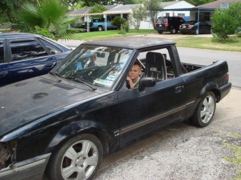 1989 Ford Escort - A black 1989 Ford Escort pickup truck is parked outside with a young boy in the driver's seat.