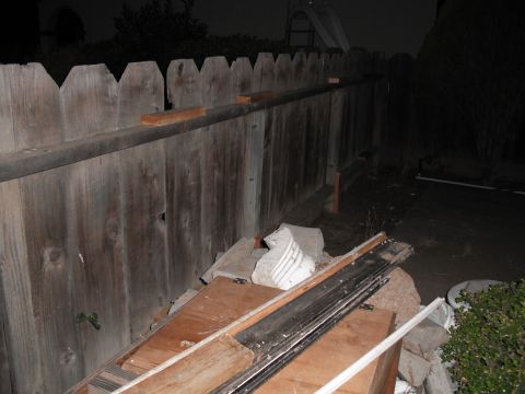 1991 Ford Bronco - Debris is piled up against a wooden fence in a backyard at night.