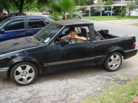 1989 Ford Escort - A young boy smiles from the driver's seat of a black 1989 Ford Escort pickup truck.