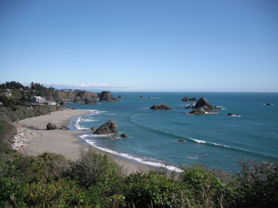 Coastal scene with a sandy beach, rocky outcroppings in the ocean, and houses on a cliff