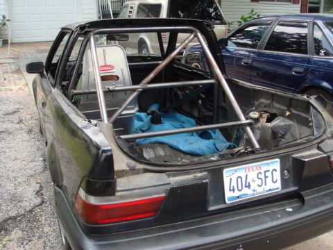 1989 Ford Escort - This car has been modified with a roll cage and racing seat, with a blue tarp covering items in the rear.