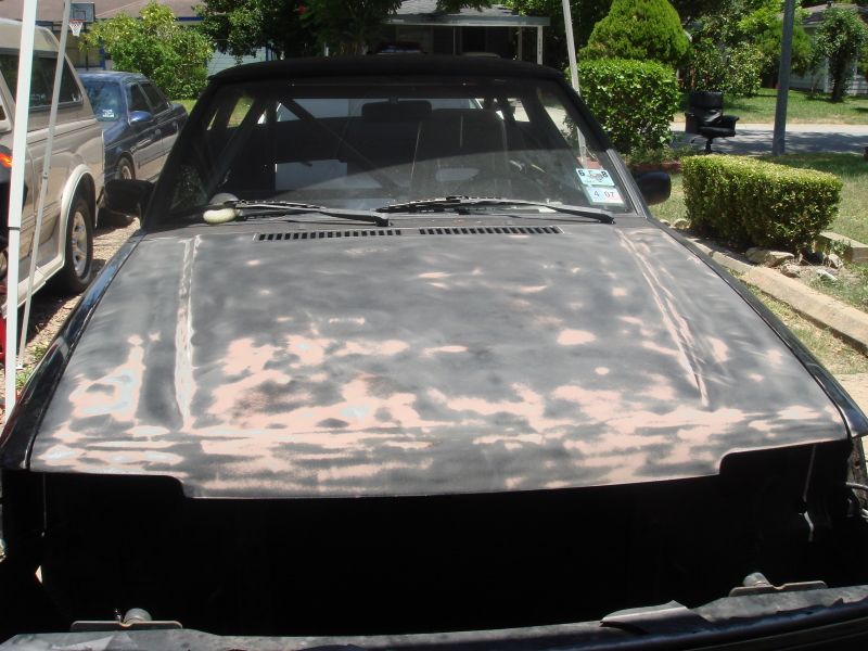 Car hood with primer and sanding marks, windshield wipers visible. Another vehicle is parked behind