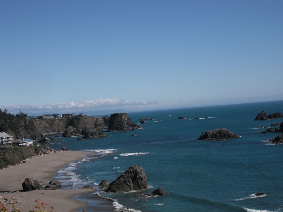 Coastal view with waves crashing on rocks and buildings on a cliff overlooking the ocean