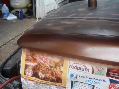 1989 Ford Escort - A car hood is covered in flyers, showing primer and a copper pipe, with a garage in the background.