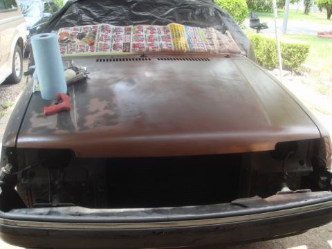 1989 Ford Escort - The front of a car is prepped for paint, with tools and supplies laid out on the hood.