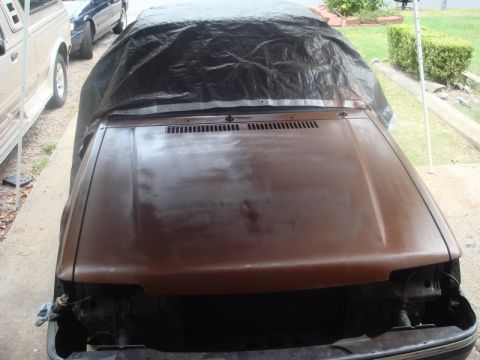1989 Ford Escort - A car's front end is partially covered by a tarp, with another vehicle parked nearby.