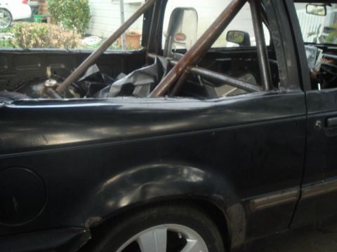 1989 Ford Escort - The interior of a black pickup truck shows a custom roll cage and a tarp covering the bed area.