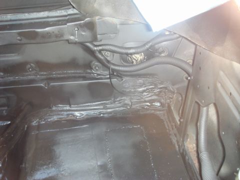 1989 Ford Escort - The interior of a car trunk shows black undercoating and protective wiring conduits.