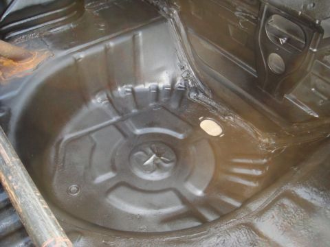 1989 Ford Escort - Underside view of a car's spare tire well, recently coated for protection.