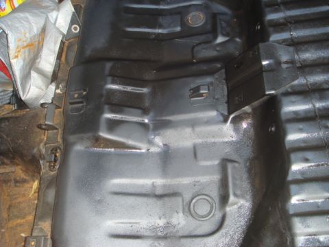 1989 Ford Escort - The undercarriage of a vehicle shows a dark, textured floor pan with various stamped shapes and mounting points.