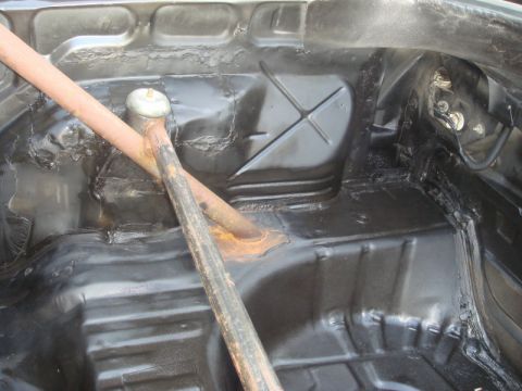 1989 Ford Escort - The interior floor of a vehicle shows a roll bar support and black undercoating.