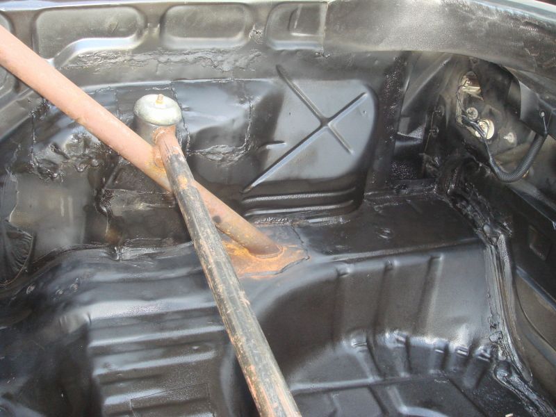 Car's rear floor pan with some rust and a roll bar support