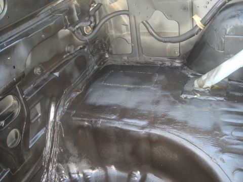 1989 Ford Escort - The interior of a car's trunk area is shown, coated in black undercoating with visible wiring and structural components.