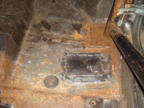 1989 Ford Escort - Close-up of a heavily rusted car interior floor with a newly welded patch and part of a roll cage visible.