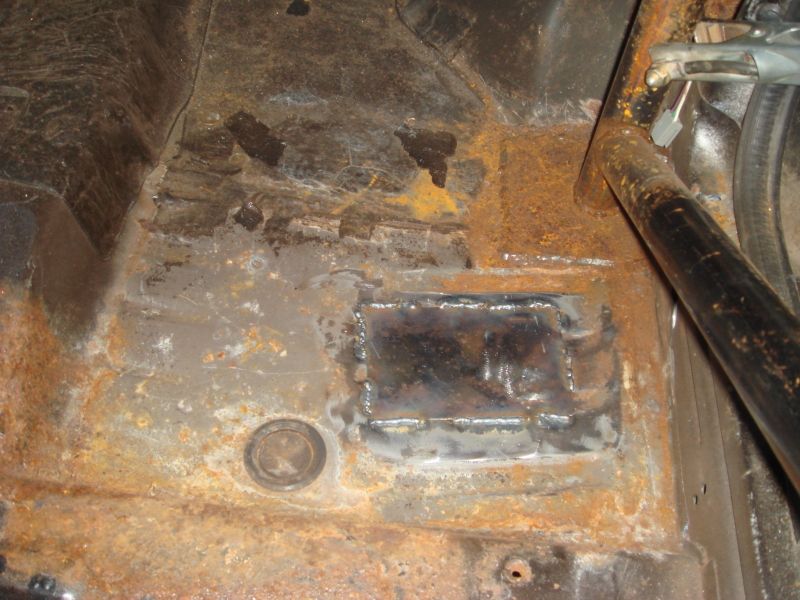 Rusted car floor with a welded metal patch and a roll bar