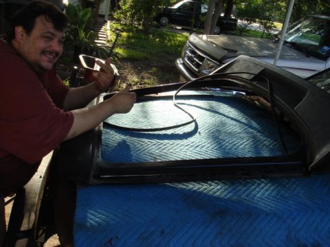 1989 Ford Escort - Man replaces a car's window seal with two trucks parked nearby.