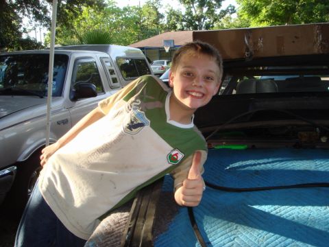 1989 Ford Escort - A smiling boy gives a thumbs up while leaning against a silver pickup truck.