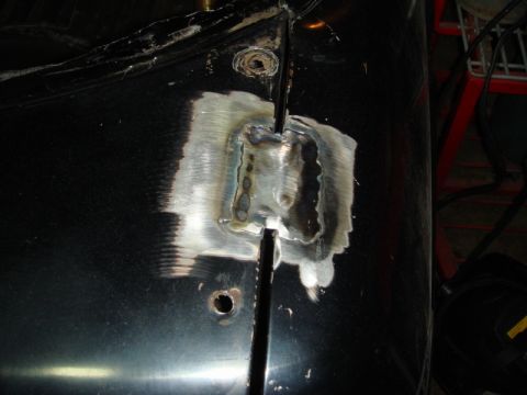 1989 Ford Escort - Close-up of a welded door hinge area on a black vehicle, showing repair work.