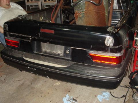 1989 Ford Escort - The rear of a black car is shown, with visible damage to the trunk and taillights, in what appears to be a garage.