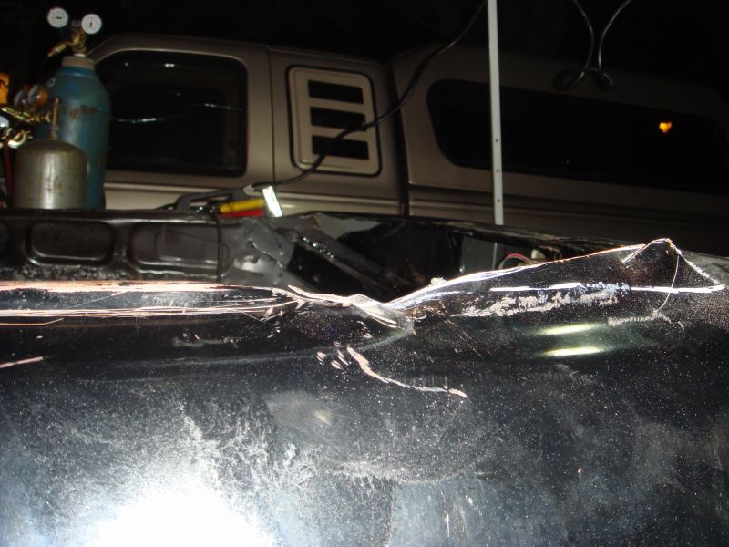 Damaged black car hood with welding sparks and a silver truck cap in the background