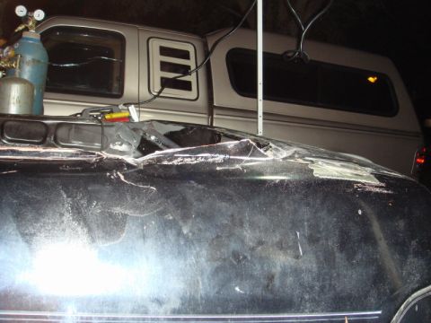 1989 Ford Escort - Welding equipment is positioned over a heavily damaged black car roof, with a silver truck visible behind it.