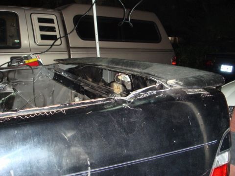 1989 Ford Escort - The rear of a car is shown with its trunk area exposed, and a truck is visible behind it.