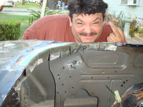 1989 Ford Escort - Man gestures with middle finger while leaning over a car's fender well during repairs.