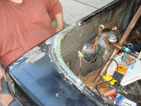 1989 Ford Escort - The interior of a car trunk is visible, with exposed wires, tools, and signs of rust and repair work.