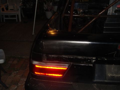 1989 Ford Escort - Rear view of a dark-colored car with a roll cage, showing the illuminated taillight.